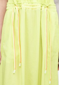 Gros plan d'une robe vert clair avec une taille froncée et deux longs cordons aux rayures orange et blanche.