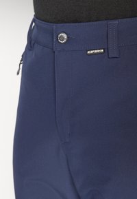 Σκούρο μπλε παντελόνι φτιαγμένο από λείο ύφασμα με κουμπί κλεισίματος, τσέπη με φερμουάρ στο πλάι και μια μικρή ετικέτα λογότυπου πάνω από την δεξιά τσέπη.