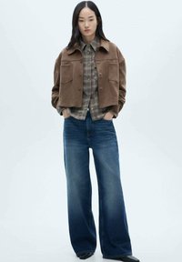 Braune Wildleder-Cropped Jacke, graues Karo-Hemd mit Knöpfen und weit geschnittene, dunkelblaue Jeans. Texturstoff mit sichtbaren Taschendetails.
