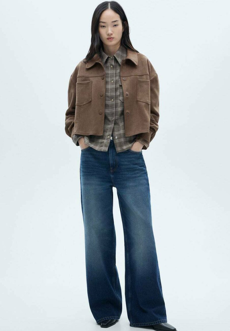 Braune Wildleder-Cropped Jacke, graues Karo-Hemd mit Knöpfen und weit geschnittene, dunkelblaue Jeans. Texturstoff mit sichtbaren Taschendetails.
