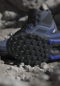 Vandringskänga med en strukturerad blå och svart ovandel, som har en robust svart sula med djupa nubb för grepp på klippiga ytor.