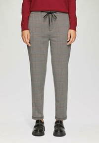 Geklede broek met een ruitpatroon in zwart, grijs en bruin, voorzien van een elastische tailleband en trekkoord. Gepaard met glanzende zwarte schoenen.