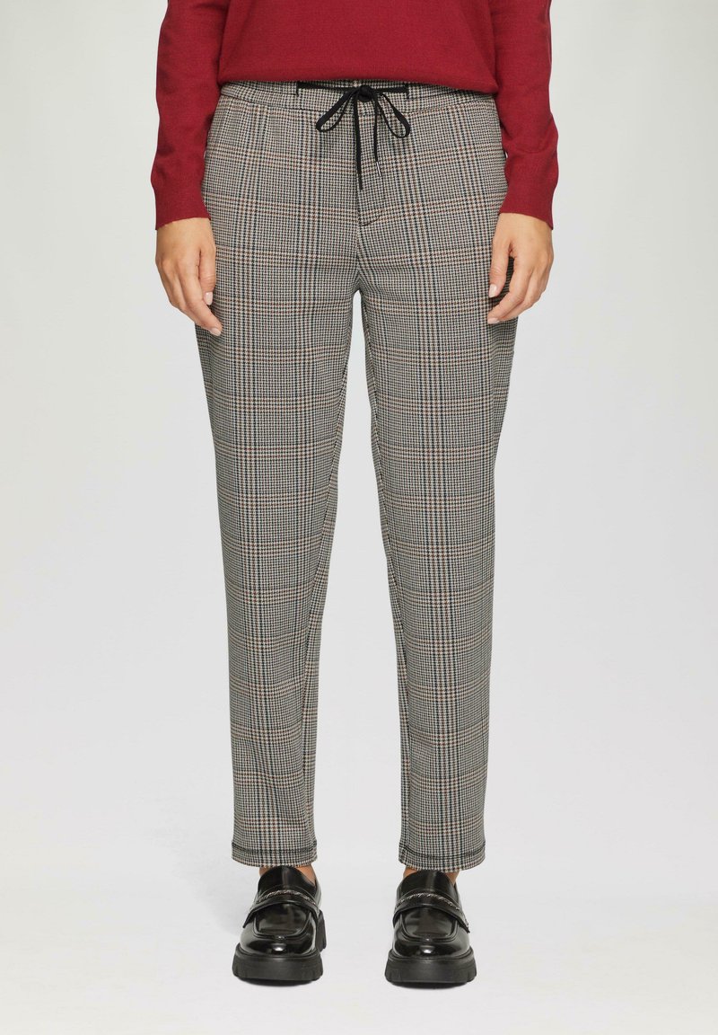 Geklede broek met een ruitpatroon in zwart, grijs en bruin, voorzien van een elastische tailleband en trekkoord. Gepaard met glanzende zwarte schoenen.
