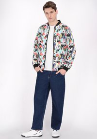 Blomstermønstret bomberjakke med pandaer, med sorte ribbede manchetter og krave, båret over en hvid t-shirt og parret med blå jeans og hvide sneakers.