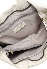 Interior de bolso de cuero beige con dos bolsillos con cremallera, un compartimento más grande y un forro de tela. Incluye una etiqueta con marca.