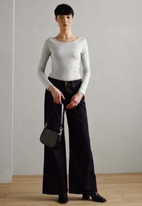 Langärmliges graues Oberteil kombiniert mit hochgeschnittenen, weit geschnittenen schwarzen Jeans. Die Accessoires umfassen eine kleine schwarze Handtasche und spitze schwarze Absätze.