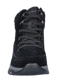 Botín de ante negro con cuello acolchado, cordones texturizados negros y suela gris. Presenta una puntera reforzada y un diseño elegante para proporcionar estabilidad.