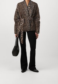 Leopardmönstrad jacka i brunt och grått, med omslagdesign och knytliv. Parat med svarta utsvängda byxor och en svart väska. Slät textur.