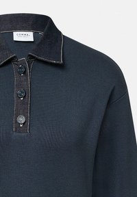 Granatowy polo w prążki z denimu, z trzema guzikami, kontrastowym przeszyciem i małą metką wewnątrz kołnierza.