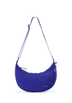 Blaue, sichelförmige Umhängetasche mit verstellbarem Träger, Reißverschluss und dezentem AEVOR-Logo vorne und seitlich.