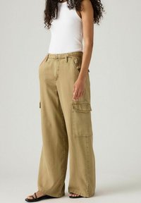 Beige brede cargo bukser med store sidelommer, en blød tekstur og diskrete syninger, parret med en tætsiddende hvid tanktop.