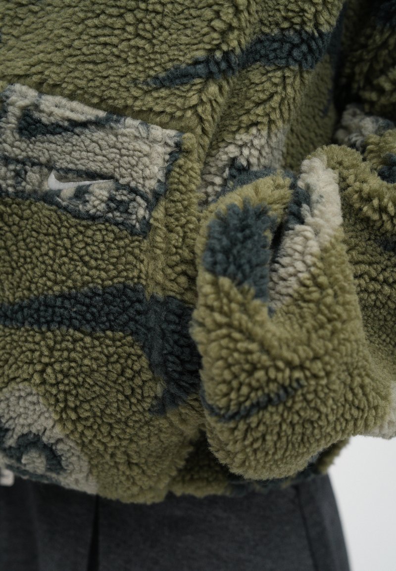 Fleecejacke in Olivgrün und Dunkelblau. Strukturierter Stoff mit plüschiger Optik, der ein markantes Muster und ein kleines Logodetail aufweist.