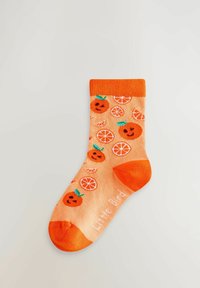 Oranžid sokid, millel on naeratavate apelsinipõhiste nägudega oranžide viilude muster ja varba lähedal tekst "Väike lind".