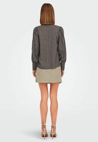 Camicia a quadri nera con maniche a palloncino, abbinata a una mini gonna a coste verde chiaro. Tacchi trasparenti completano l'outfit.