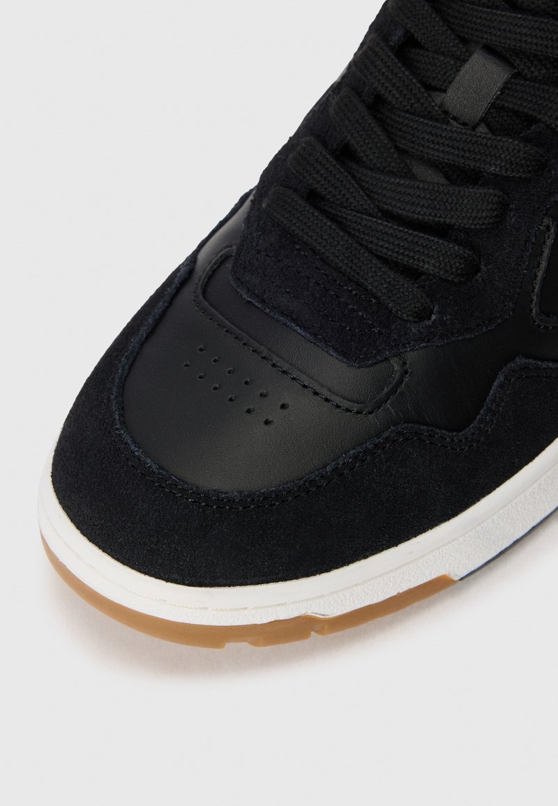 Schwarzer Sneaker mit Obermaterial aus Wildleder und Leder, flachen Schnürsenkeln, durchlässigem Zehenbereich und Sohle aus Gummigemisch. Glatte, strukturierte Oberflächen mit detaillierter Naht.