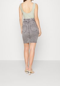 Grijze denim rok met een aansluitende vorm en achterzakken, gecombineerd met een lichtgroene tanktop met een lage achterkant.