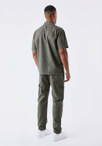 Camicia a maniche corte verde oliva con colletto e pantaloni cargo abbinati realizzati in tessuto leggero, dotati di tasche laterali e vestibilità comoda.