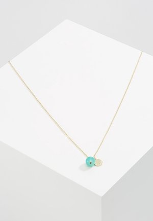 Delikat guldkæde med en rund turkisperle og en lille gylden cirkulær charme på en hvid overflade.