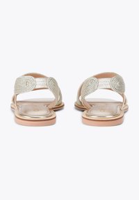 Gold flat sandals featuring woven straps with spiral accents, a smooth insole, and a tan outsole. Designed without a heel.