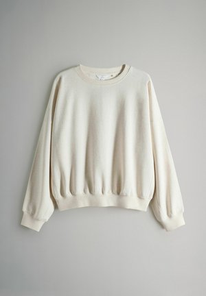 Bluza w kolorze kremowym z okrągłym dekoltem, obniżonymi ramionami, ściągaczami na mankietach i w pasie. Wykonana z miękkiej tkaniny o delikatnie fakturowanym wykończeniu.