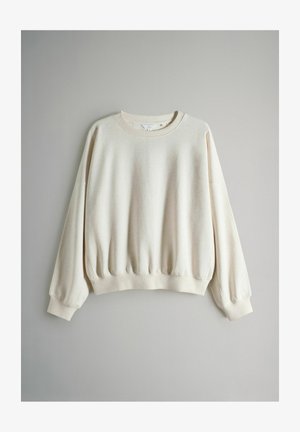 Bluza w kolorze kremowym z okrągłym dekoltem, obniżonymi ramionami, ściągaczami na mankietach i w pasie. Wykonana z miękkiej tkaniny o delikatnie fakturowanym wykończeniu.