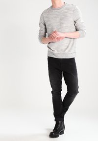 Suéter gris texturizado con cuello redondo, combinado con jeans negros y botas negras con cordones. Atuendo elegante y casual con un corte moderno.