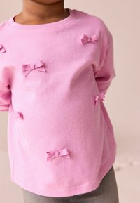 Lyserød bomuldssweatshirt med flere teksturerede båndsløjfer i forskellige størrelser, rund halsudskæring og lange ærmer.