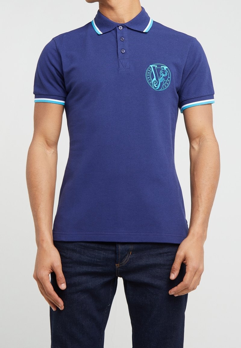 Polo shirt bleu marine en mélange de coton à manches courtes. Présente des accents bleu clair sur le col et les manches, ainsi qu'un logo brodé sur la poitrine.