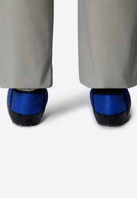 Calzature blu e nere con suole testurizzate, parzialmente coperte da pantaloni grigi. Le scarpe hanno un design aerodinamico e una linguetta sul retro.