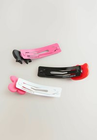 Tre färgglada hårspännen är arrangerade på en ljus bakgrund: ett svart spänne med röd accent, ett rosa spänne och ett vitt spänne med en rosa design.
