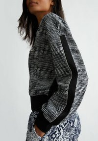 Maglione a trama in bianco e nero con design cropped, dotato di pannelli laterali in satin nero e polsi a costine. Tessuto stampato, silhouette aderente.