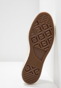 Podeszwa beżowego sneakersa Converse All Star, pokazująca teksturowaną brązową gumę z wzorami w diamenty i gwiazdy, rozmiar 42 oznaczony na podeszwie.