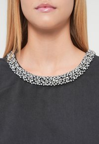 Top negru cu decolteu rotund, decorat cu o serie detaliată de paiete transparente asemănătoare bijuteriilor, creând un efect texturat și sclipitor.