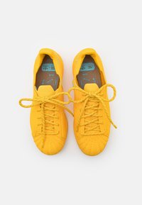 Ljusa gula sneakers med texturerat tyg, rund tå och gula snören. Insidan har sulor med blått mönster.