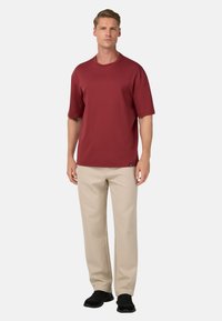 Burgunderfarbenes, kurzärmeliges T-Shirt und beiger Hosen. Das T-Shirt hat einen Rundhalsausschnitt und einen lässigen Schnitt; die Hose hat einen geraden Beinverlauf mit Seitentaschen.