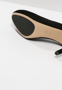 Black suede high-heeled shoe with a rounded toe and a smooth inner sole. Features a black rubber outsole for grip and stability.