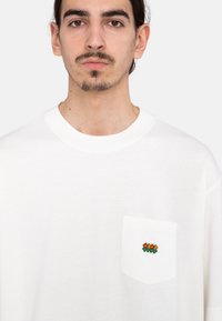 White cotton t-shirt featuring a chest pocket with colorful flower embroidery. Classic crew neckline and relaxed fit. Smooth texture.
