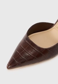 Mules à talons hauts en cuir marron avec un motif crocodile, bout pointu et talon ouvert. L'intérieur est doublé d'un beige lisse.