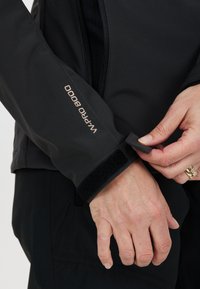 Svart vattentät jacka med justerbar manschett som har ett velcro-band och präglad "WP PRO 8000" detalj på ärmen. Slät, funktionell design.