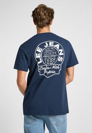 Marinblå t-shirt i bomull med en vit grafik på baksidan med "Lee Jeans" och annan text, rund logotypform, korta ärmar.