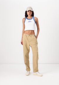 Hvid crop top med blå detaljer og logo; beige cargo bukser med en afslappet pasform; beige kasket; hvide sneakers med lyse detaljer.