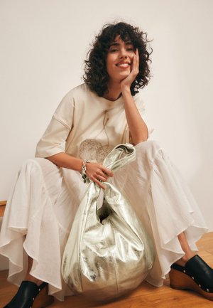 Metallic sidabrinės spalvos hobo tipo rankinė, didelio dydžio; modelis vilki kreminės spalvos viršų su vyšnių raštu ir plačias balton skeltuvas kelnes.