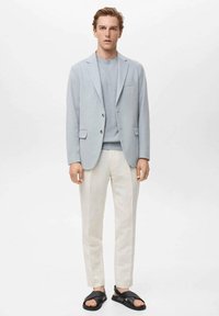 Light blue blazer with a textured finish, paired with a light blue sweater, white trousers, and black sandals. Simple design with minimal details.