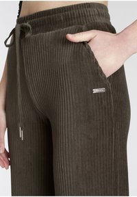 Olive green corduroy pants with vertical ribbing, elastic waistband, drawstring, side pockets, and a small metallic logo accent.