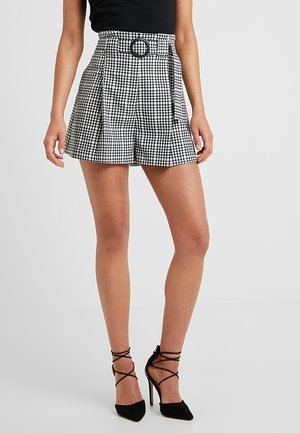 Pantaloni shorts a scacchi bianco e nero con vita alta, pieghe e una cintura con fibbia circolare; abbinati a tacchi neri con cinturini.