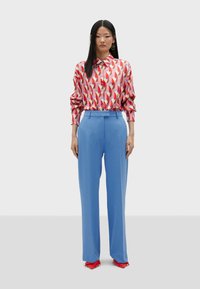 Red and pink patterned blouse with a collar, paired with tailored blue pants. Bright red pointed-toe shoes. Smooth, lightweight fabric.