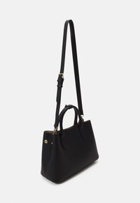 Sac à main en cuir noir avec des poignées courtes et une longue bandoulière réglable, présenté en angle trois quarts sur un fond uni.