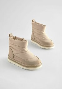 Beige synthetische enkellaarsjes met een gevoerde bovenkant, een ronde neus en een witte tussenzool. Kenmerkt zich door gestikte details en een aantreklip voor gemakkelijk aan- en uittrekken.