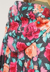 Tkanina w kwiatowy wzór w wielokolorowych odcieniach różu, pomarańczu i turkusu na ciemnym tle; posiada kaptur i detale z guzikami.