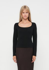 Haut noir à manches longues avec un décolleté carré, design ajusté et texture lisse. Associé à une jupe marron foncé.